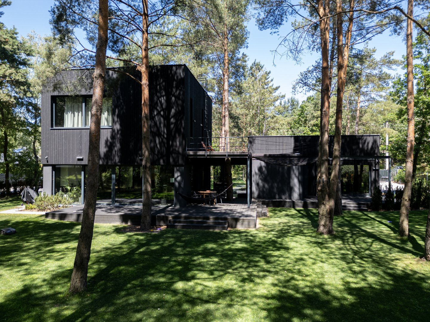 Nowoczesny dom jednorodzinny z ciemnym dachem zbudowany przez New-House na zalesionej działce – widok z lotu ptaka.